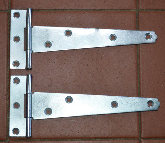 Pair of 6-inch zinc plated light duty tee hinges on brown tiled surface for sheds and gates