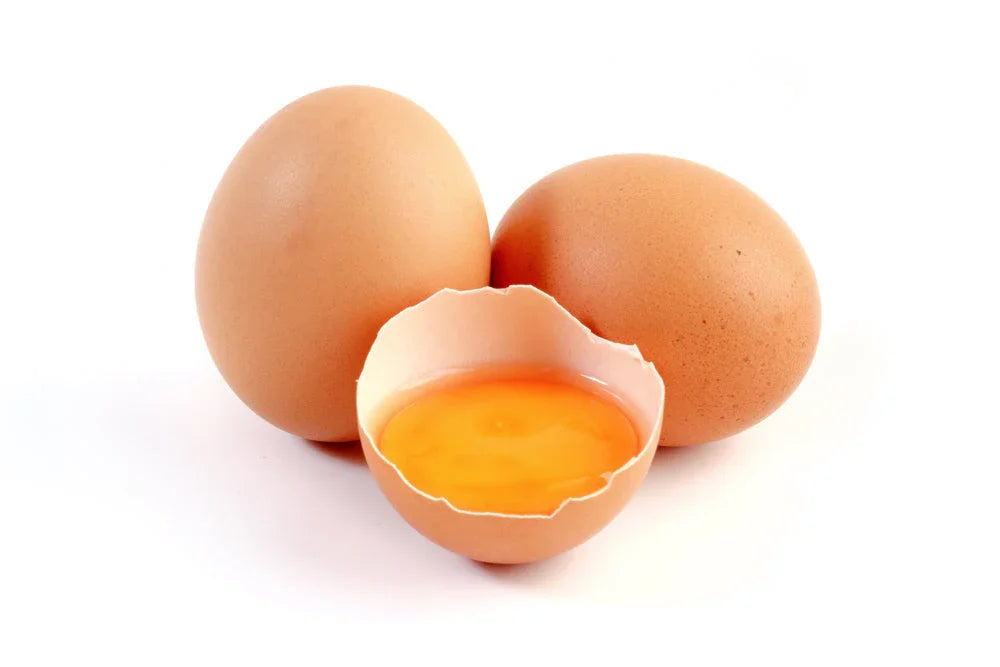 Two whole brown eggs and one cracked egg with yolk on white background